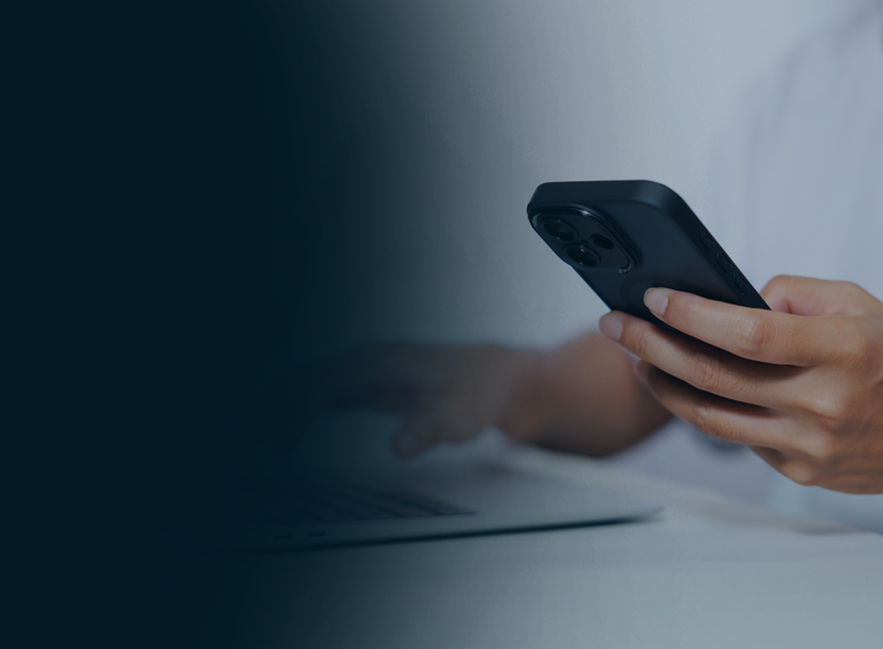Person using a smartphone with a laptop in the background